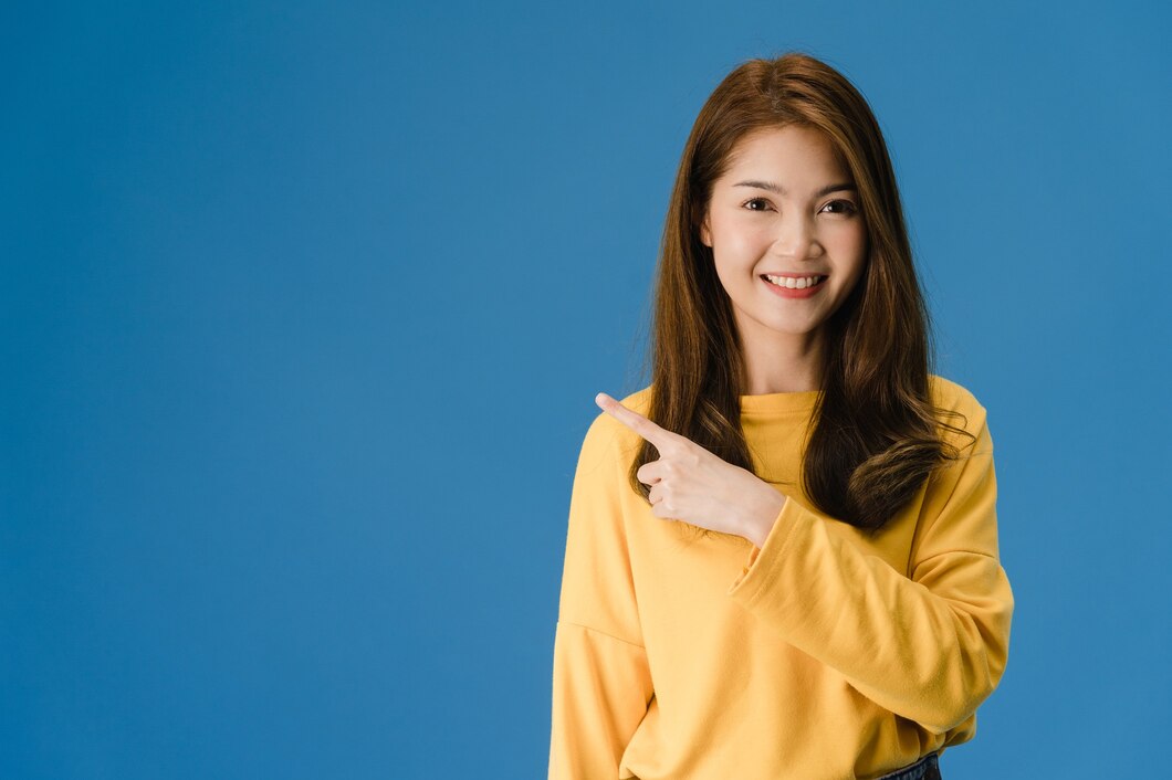 Portrait Young Asian Lady Smiling With Cheerful Expression Shows Something Amazing Blank Space Casual Clothing Looking Camera Isolated Blue Background Facial Expression Concept 7861 2720